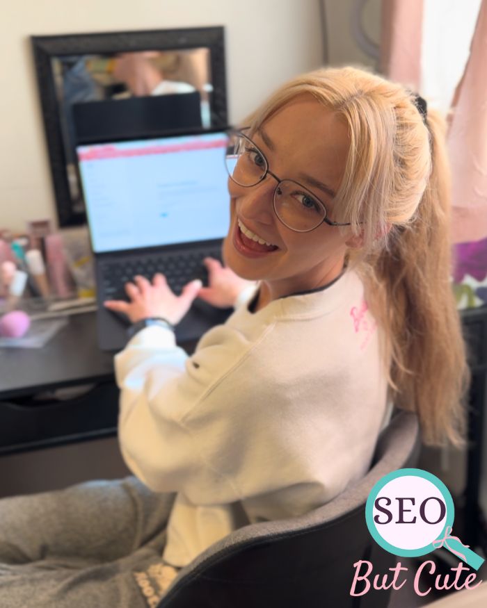 Young blonde woman sitting and smiling over her shoulder, in front of a laptop